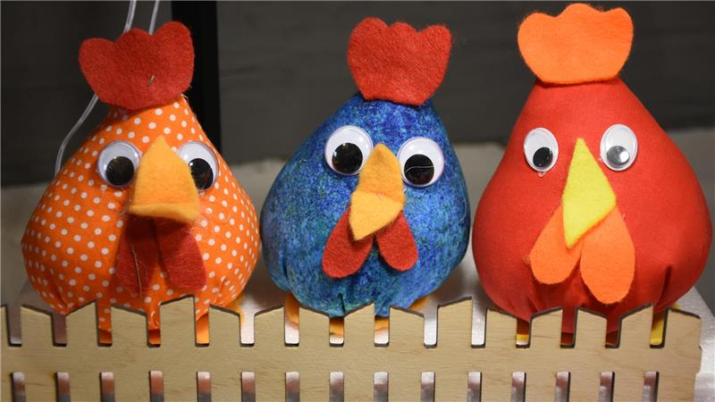 Drei bunte Stoff-Hühner hinterm Lattenzaun.