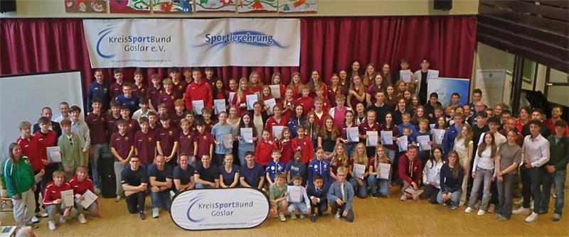 Große Gruppe von Menschen in einer Halle vor zwei Bannern mit den Aufschriften 'KreisSportBund Goslar e.V.' und 'Sportlerehrung'