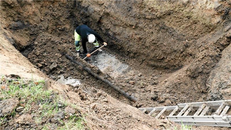 Ein Mann mit Schaufel legt in einem Loch eine Leitung frei.