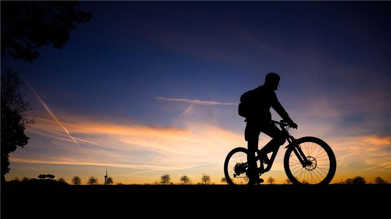 Fahrradfahrer im Morgengrauen: Silhouette vor Sonnenaufgangshimmel in Hannover.