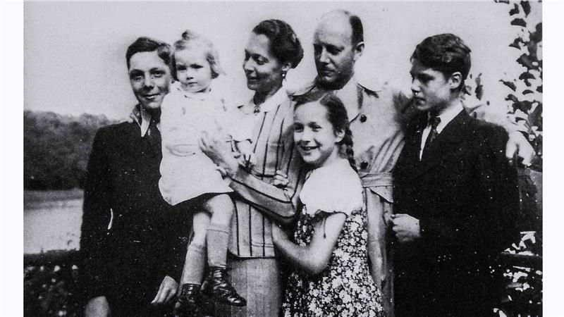 Schwarz-weiße Aufnahme einer Gruppe von sechs Personen, darunter zwei Kinder, die eng beieinander stehen und in Richtung Kamera blicken