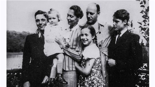 Schwarz-weiße Aufnahme einer Gruppe von sechs Personen, darunter zwei Kinder, die eng beieinander stehen und in Richtung Kamera blicken