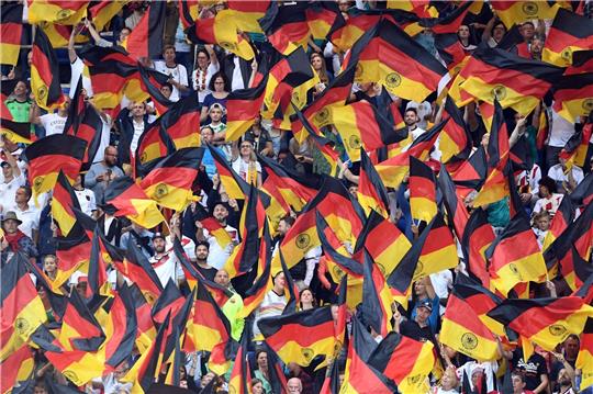 Fans schwenken Deutschlandfahnen auf der Tribüne.