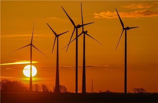 Farbenprächtig geht die Sonne über der Landschaft in Ostbrandenburg mit mehreren Windrädern auf.