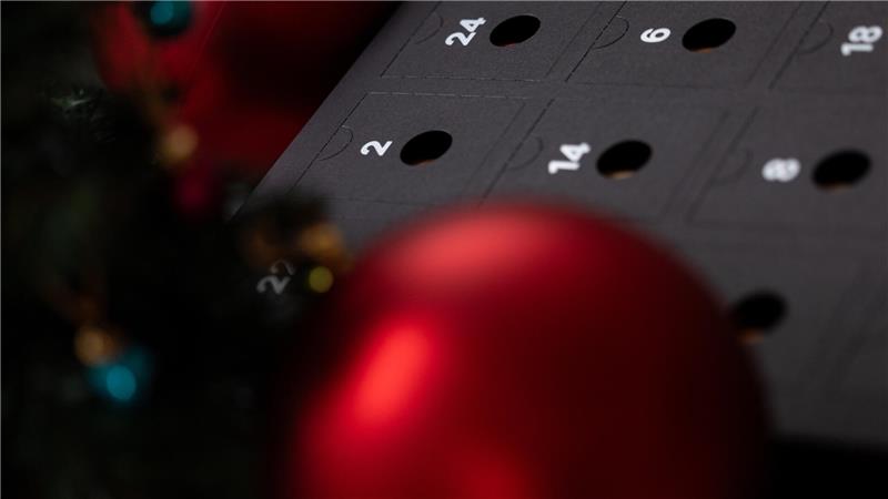 Ein schwarzer Kalender umgeben von roten Weihnachtskugeln.