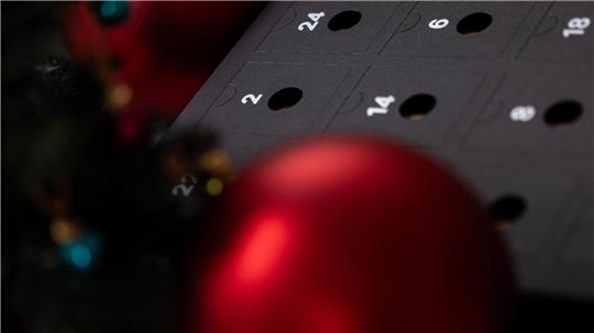 Ein schwarzer Kalender umgeben von roten Weihnachtskugeln.