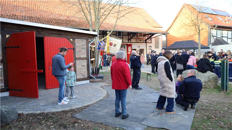 Menschen stehen und sitzen vor einem Fachwerkhaus mit offenem roten Tor an einem sonnigen Tag