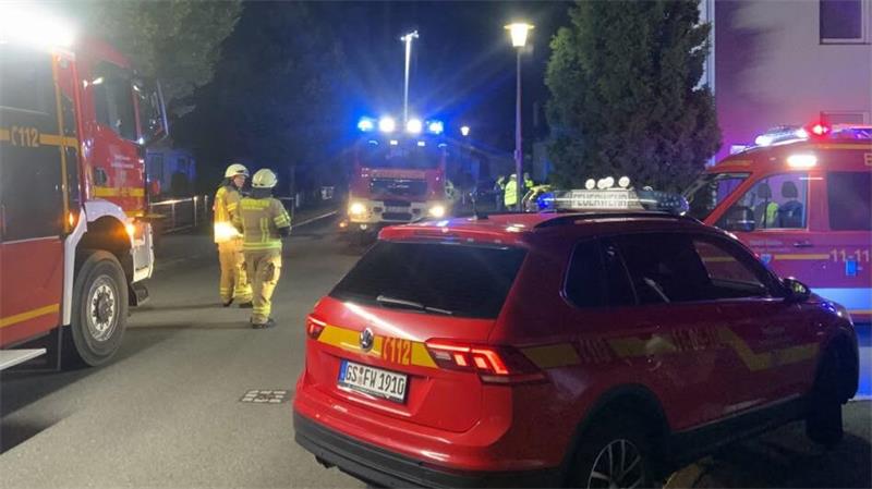 Feuerwehrfahrzeuge und Feuerwehrleute am Abend auf einer Straße, die hell ausgeleuchtet ist.