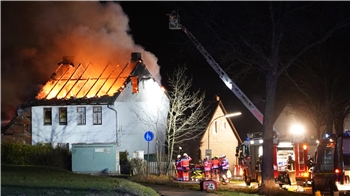 Ein brennender Dachstuhl in der Nacht und Feuerwehrleute sowie eine Drehleiter und Feuerwehrfahrzeuge.