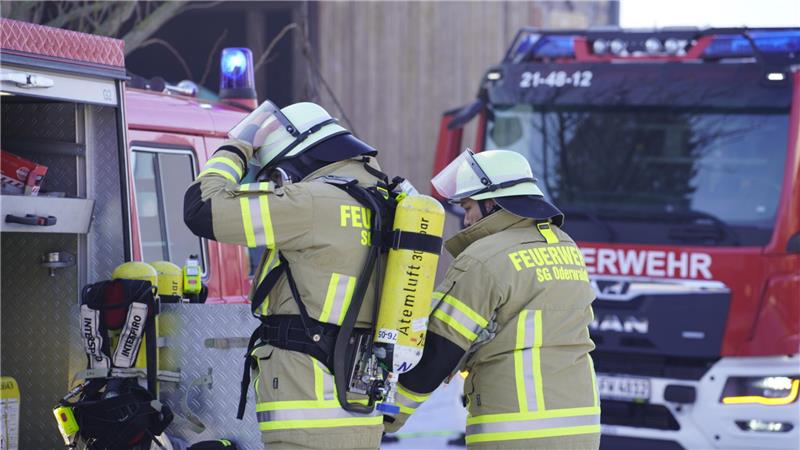 Zwei Feuerwehrleute stehen an einem geöffneten Fahrzeug und rüsten sich mit Sauerstoffflaschen aus.
