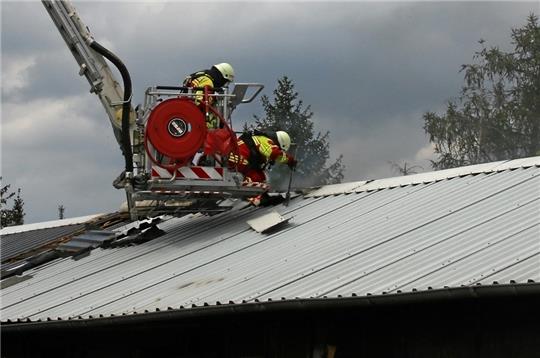 Feuerwehrkräfte öffnen das Blechdach der Wohnbaracke, um Glutnester zu finden und abzulöschen. Fotos: Leifeld