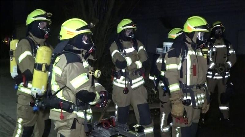 Feuerwehrleute mit Atemschutzmasken stehen vor dem Mehrfamilienhaus in Ronnenberg.