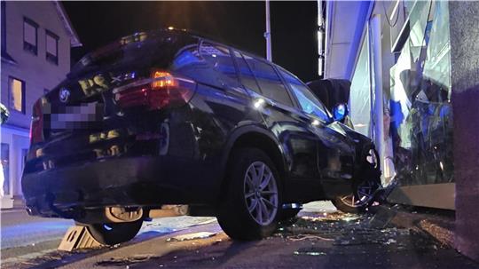 Ein schwarzer BMW steht vor einer großen Scheibe, die er kurz zuvor zerstört hat.