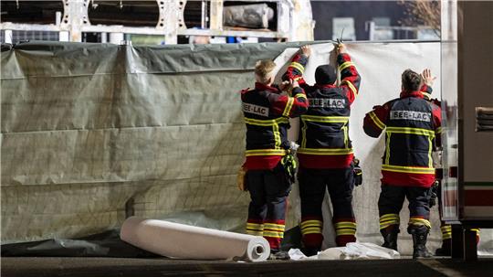 Feuerwehrleute verdecken den ausgebrannten Bus.