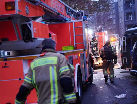 Feuerwehrmänner laufen auf der Schudomerstraße in Berlin-Neukölln zu den Einsatzfahrzeugen.