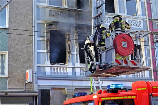 Feuerwehrmänner stehen vor dem Mehrfamilienhaus, in dem es gebrannt hat.