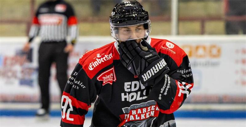 Eishockeyspieler in schwarzem Trikot mit roten und weißen Details auf dem Eis, trägt Helm und Handschuhe, hält Schläger.