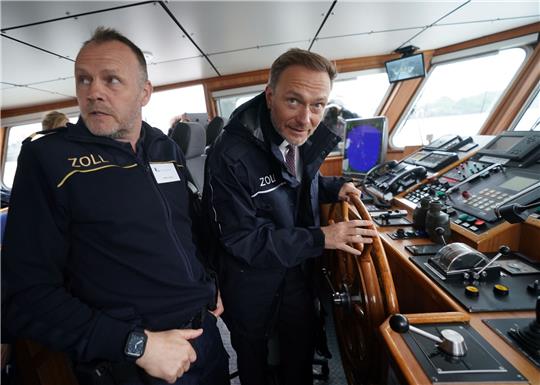 Finanzminister Christian Lindner (r)  steuert das Zollboot «Kehrwieder», links Zollkapitän Steffen Molter.