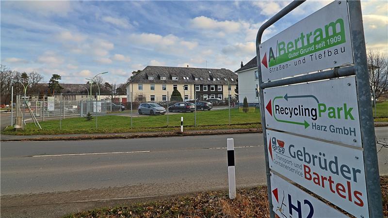 Schild mit Firmenlogos und Richtungspfeilen vor einer Straße, im Hintergrund ein mehrstöckiges Gebäude und geparkte Autos.