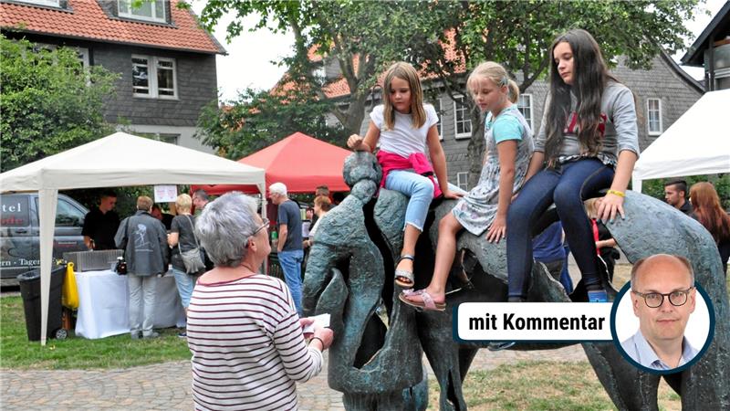 Drei Kinder sitzen und klettern auf einer bronzenen Skulptur von zwei Pferden in einem Park mit mehreren Menschen auf Bänken und einem Kinderwagen im Hintergrund