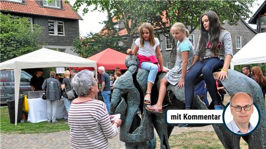 Drei Kinder sitzen und klettern auf einer bronzenen Skulptur von zwei Pferden in einem Park mit mehreren Menschen auf Bänken und einem Kinderwagen im Hintergrund