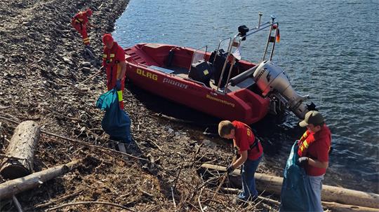Menschen in roten DLRG-Uniformen sammeln Müll am Ufer neben einem roten Rettungsboot