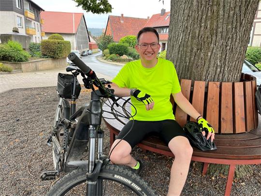Ein Mann sitzt in Fahrradkleidung auf einer Bank. Vor ihm steht sein Rad.