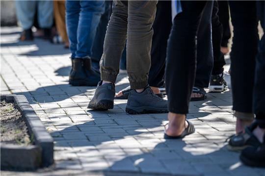 Flüchtlinge stehen in einer Erstaufnahme-Einrichtung in einer Schlange (Symbolbild). Der Stadtrat von Burg fordert im Brief an Kanzler Scholz unter anderem eine Rückführung abgelehnter Asylbewerber und eine Erweiterung der sicheren Herkunftsländer.