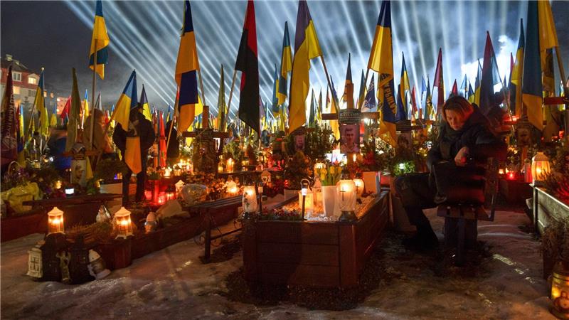 Flutlichter leuchten in Lwiw über den Gräbern der gefallener Soldaten, während Menschen am Vorabend des vierten Jahrestages der russischen Invasion Kerzen anzünden.