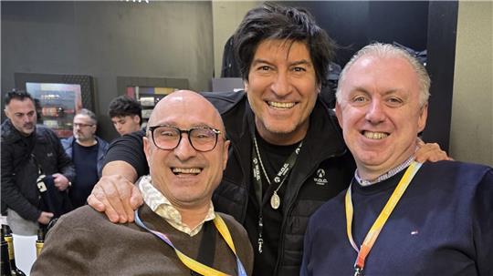 Das Foto zeigt zwei Männer, die von einem dritten umarmt werden.