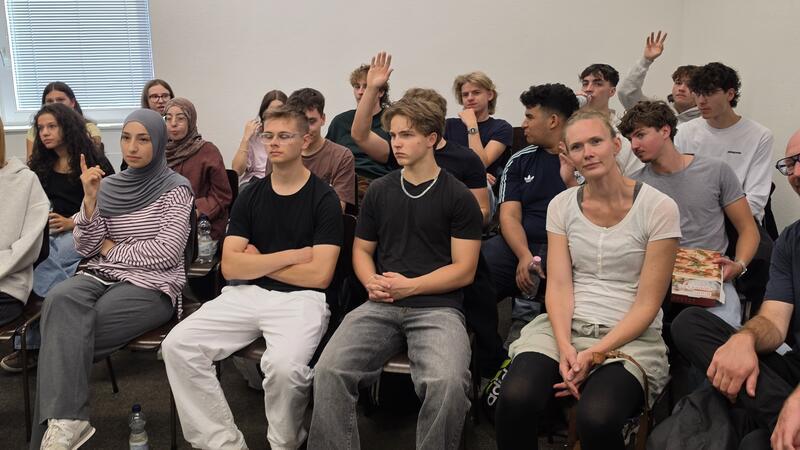 Mehrere Schüler sitzen auf Stühlen nebeneinander.