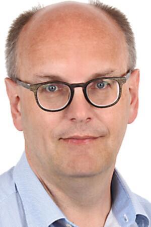 Mann mit kurz geschnittenem, lichtem Haar trägt hellblaues Hemd mit offenem Kragen.