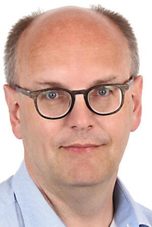 Mann mit kurz geschnittenem Haar und hellblauem Hemd mit offenem Kragen vor weißem Hintergrund