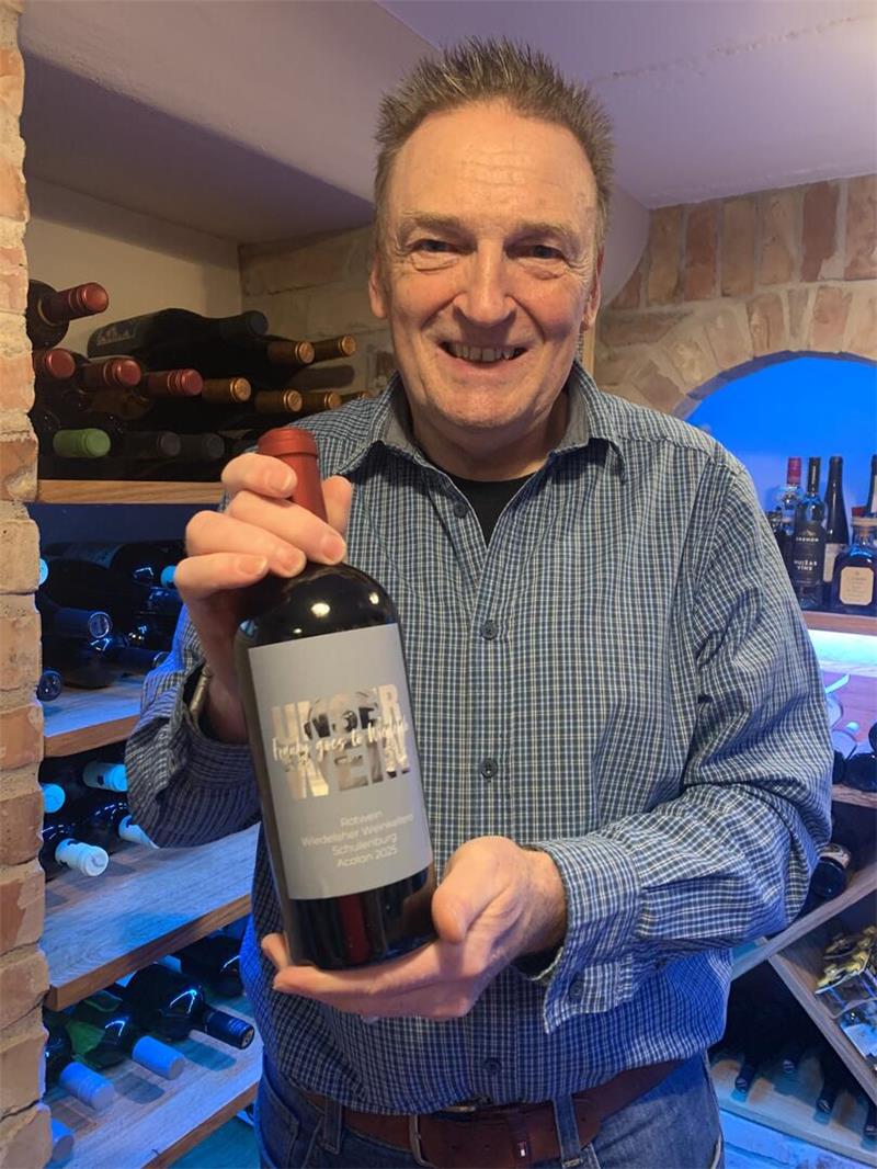 Wie Frank Schulenberg vom Genießer zum Hobbywinzer wurde Mann in kariertem Hemd hält eine große Weinflasche in einem Weinkeller mit Regalen voller Weinflaschen