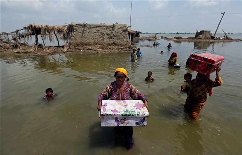 Frauen tragen Habseligkeiten aus ihrem durch heftige Regenfälle überschwemmten Haus im Bezirk Qambar Shahdadkot in der pakistanischen Provinz Sindh.