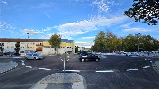 Kreisverkehr mit neu asphaltierter Fahrbahn und Verkehrsinsel in einer Wohnsiedlung mit mehrstöckigen Wohnhäusern und Bäumen im Hintergrund