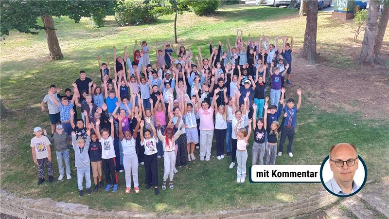 Große Gruppe von Kindern und Jugendlichen steht auf einer Wiese und hebt die Arme nach oben