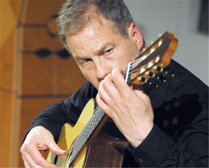 Mann in schwarzem Oberteil spielt klassische Gitarre.