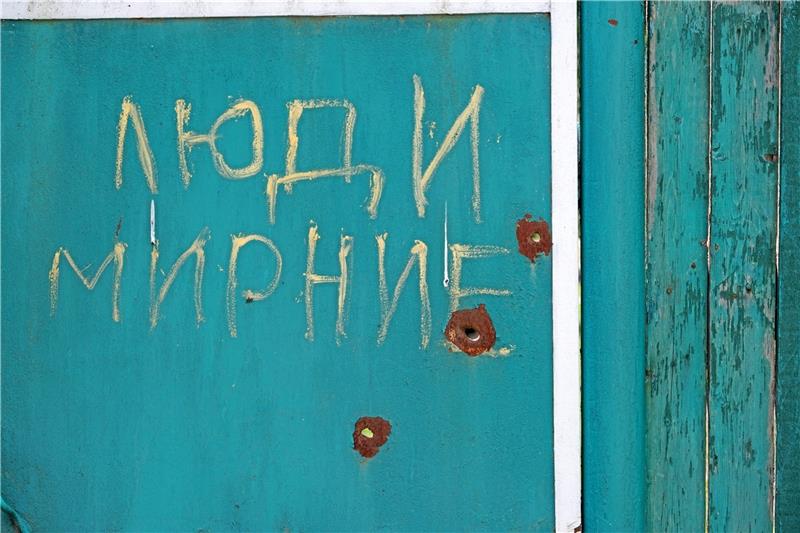 Reise in die Ukraine: Wiederaufbau als Akt des Widerstands „Friedliche Menschen“ steht an einer Hofeinfahrt in dem ukrainischen Dorf Lukashivka in russischer Schrift. Darunter sind Einschusslöcher zu sehen. Ein weiterer Schriftzug weist darauf hin, dass Kinder in dem Gebäude leben. Foto: Privat