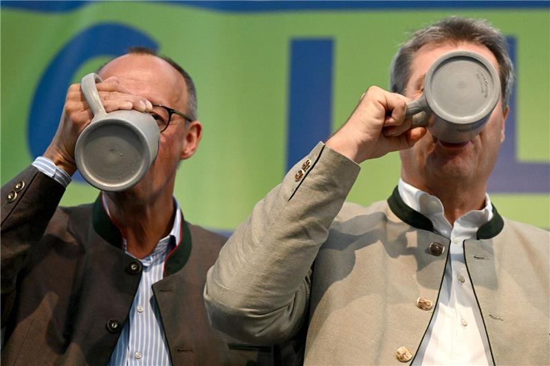 Im Bierzelt - Merz, Aiwanger und Klingbeil beim Gillamoos Friedrich Merz (l), Bundesvorsitzender der CDU, und Markus Söder (CSU), Ministerpräsident von Bayern, trinken beim Politischen Frühschoppen Gillamoos auf der Bühne aus Bierkrügen.