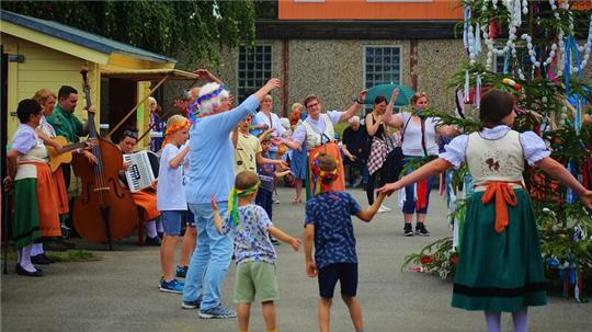 Fröhlich tanzen die Kinder und Erwachsenen auf dem Gelände am Gemeindehaus um den Johanni-Baum.