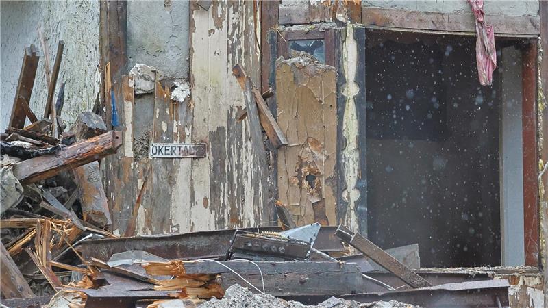 Verfallenes Gebäude mit abgeblättertem Putz, offenem Fenster und Trümmern davor