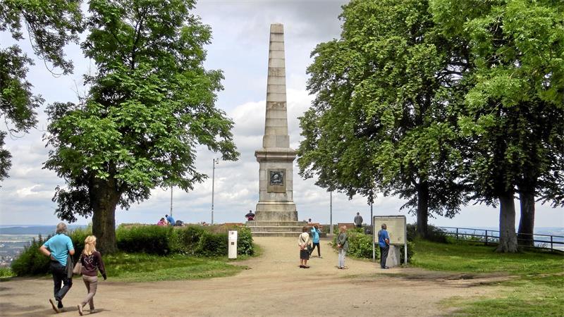 Das Bild zeigt eine Steinsäule mit mehreren Menschen davor.