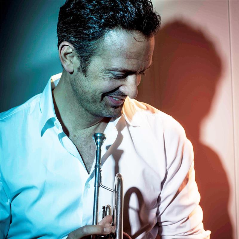 Ein Mann mit Trompete sieht lächelnd zu Boden.