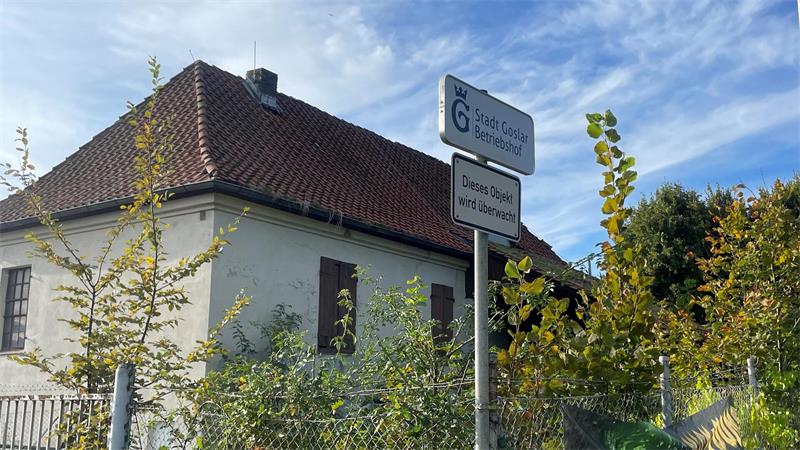 Haus mit rotem Ziegeldach und zwei Verkehrsschildern vor grünem Buschwerk unter blauem Himmel