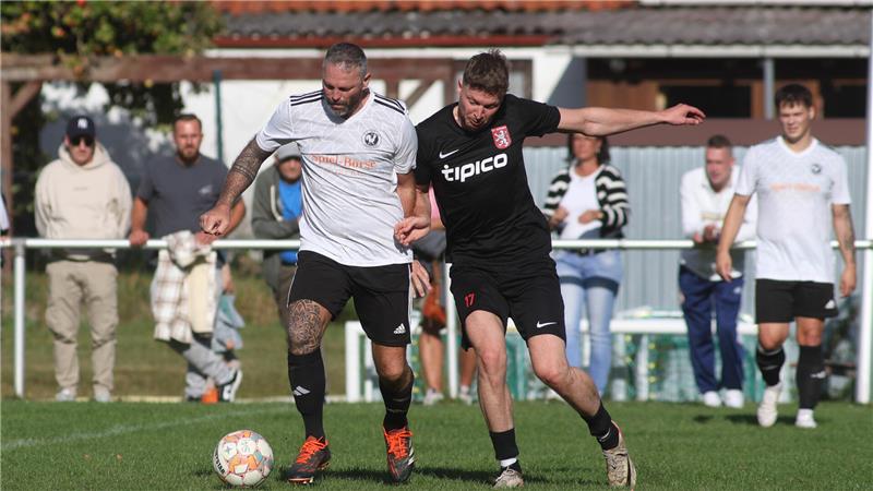 Zwei Fußballspieler kämpfen um den Ball auf einem Spielfeld vor Zuschauern hinter einem Zaun