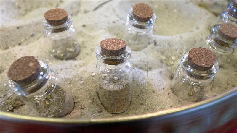 Mit Sand und goldfarbenen Staub gefüllte Gläschen stecken in einer Sandschüssel.