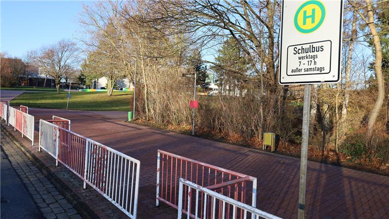 Haltestellenschild mit der Aufschrift 'Schulbus' an einem Gehweg mit weißen Metallzäunen und kahlen Bäumen im Hintergrund