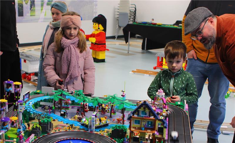 Ein Mädchen und ein Nunge betrachten eine Lego-Landschaft. Ein Mann blickt dem Jungen über die Schulter.