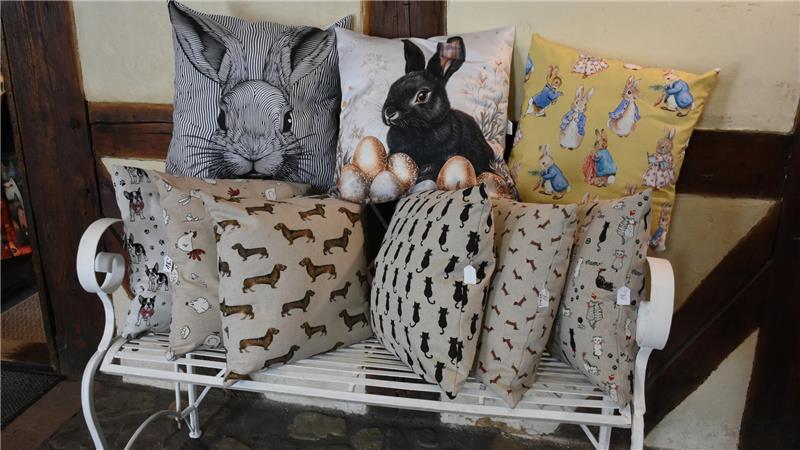 Auf einer weißen Metallbank sind Kissen mit tierischen Bezügen drapiert. Ganz oben: Osterhasenmotive.